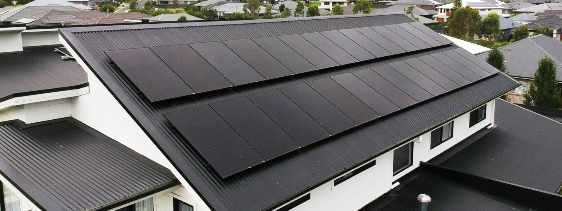 Aerial view of large black solar panel array on a dark roof